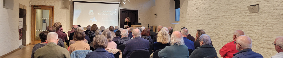 people watching a woman present a talk with a presentation on a board at the back of the room